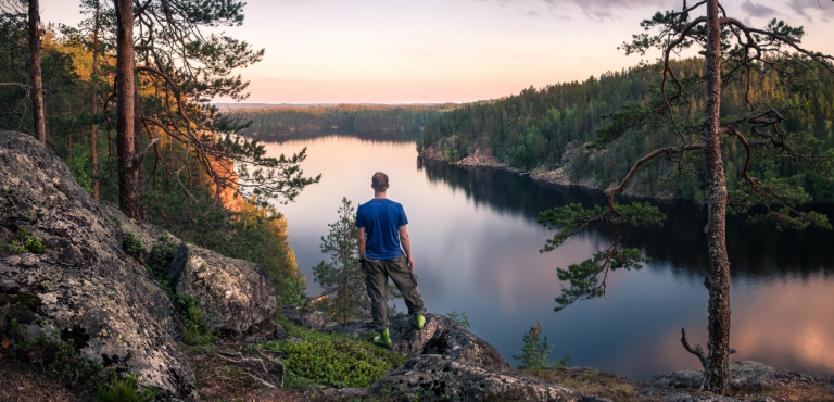 Kuvassa retkeilijä katsoo suomalaista järvimaisemaa korkealta kalliolta.